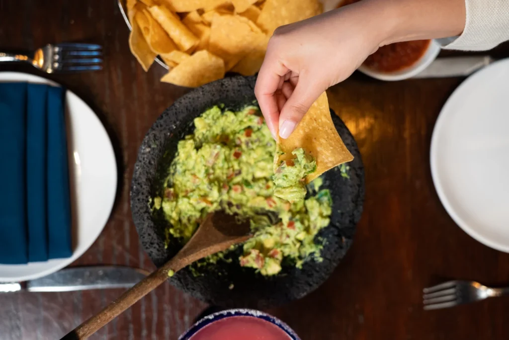 A tables with tortilla chips and a hand dipping into guacamola en molcajate